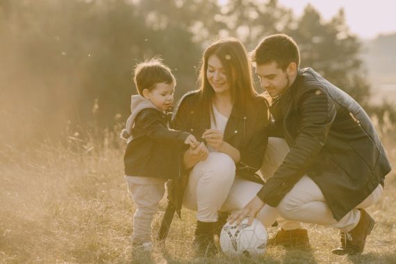 A cheerful family bonding outdoors with a soccer ball, enjoying a sunny day in the grass.