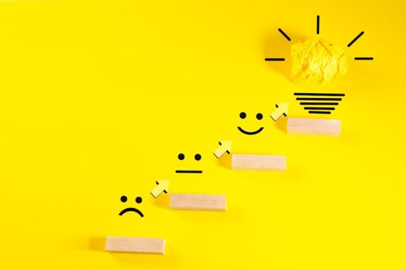 Creative idea concept. Wooden blocks with smiley face and light bulb on yellow background.